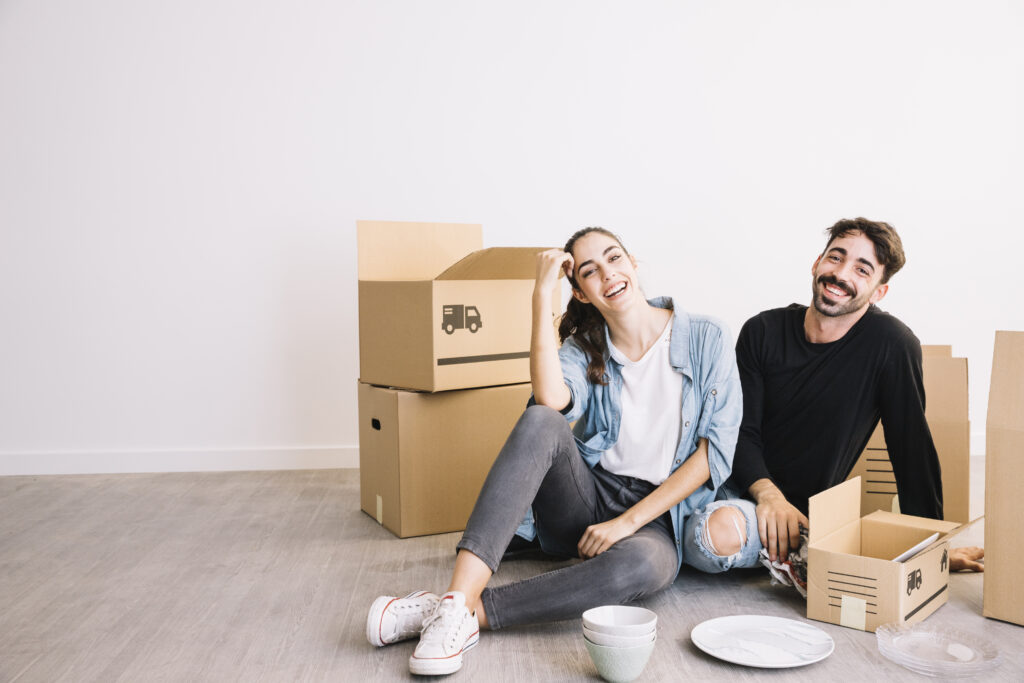 a young couple happy and smiling in a rented apartment with packing boxes beside them